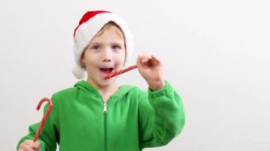 Noel Baba şapkalı, karamel çubuklu bir çocuk. Elinde hediyesiyle Noel şapkalı bir çocuk. Yüksek kalite 4k görüntü