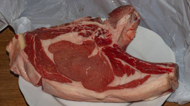 Beyaz bir tabakta sunulan, mermer ve renk bakımından zengin çiğ bifteğin birinci sınıf kesimi, aşçılık hazırlığı için hazır.