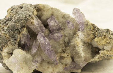 Küçük, ham ametist kristallerinin, şeffaf mor renkte, karmaşık bir şekilde kayalık matrislerine gömülmüş, jeolojik harikaları ortaya çıkaran yakın çekim görüntüsü.