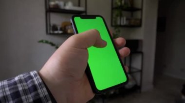 Yeşil ekranlı akıllı telefonu kapatın ve odada otururken kaydırın. Elinde krom anahtarla siyah cep telefonu tutan adamlar, teknoloji kavramı. Video 4K
