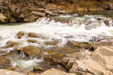 Ukrayna Karpatları 'nda manzaralı bir bahar şelalesi. Büyük kahverengi kayaların arasında güzel bir nehir akıyor..