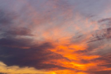 Akşam gökyüzü, gün batımında turuncu, mor ve kırmızıya boyanmış. Parlayan bulutlar soyut bir doğal doku oluşturur, arka plan veya ilham verici görseller için idealdir..
