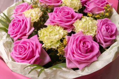 Soluk yeşil karanfillerle çevrili canlı pembe bir gülün yakın çekimi. Çiçek, romantik ve doğa teması için mükemmel..