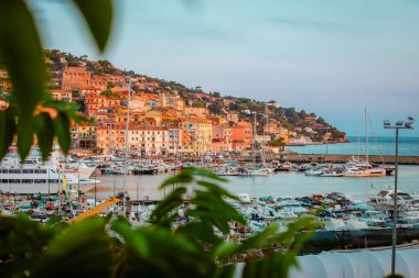 Porto Santo Stefano, İtalya - 21 Ağustos 2024: Porto Santo Stefano 'nun ağaç yaprakları arasından gün doğumunda panoramik manzarası