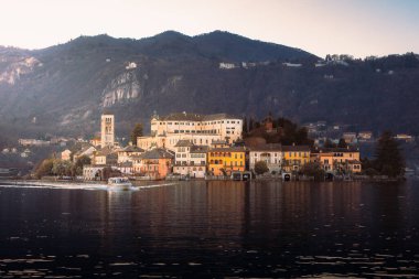 Orta San Giulio, İtalya - 29 Aralık 2024: Orta Gölü 'ndeki San Giulio adasının gün batımında turist taşıyan turist teknesiyle görüntüsü