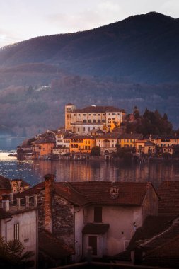 Orta San Giulio, Italy - 29 December 2024: The iconic island of San Giulio as seen from the lakeside promenade in Orta San Giulio, vertical clipart