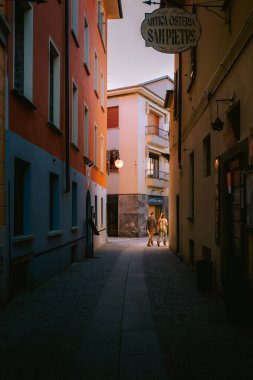 Verbania, İtalya - 3 Mayıs 2025: Geleneksel bir İtalyan kasabasında günlük hayatın cazibesini yakalayan renkli binalar, balkonlar ve insanlar ile İtalya 'nın tarihi iç kesimlerinde dar bir ara sokak