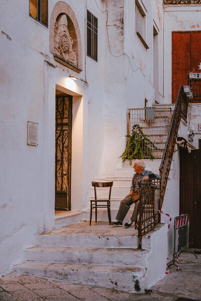 Oria, Brindisi - 7 August 2025: Elderly men sitting outside social club in Oria historic center, chatting and relaxing on a warm summer afternoon