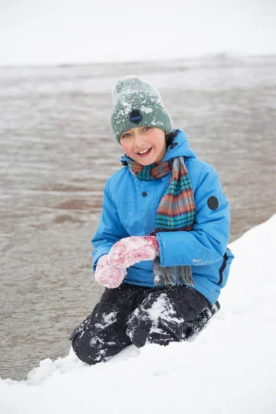 A boy in a snow-covered park on the riverbank. A photo of a teenager in a winter forest. Winter, winter holidays, vacation holidays.
