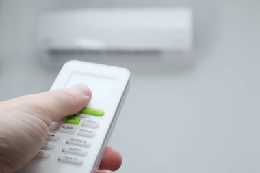 Uzaktan kumanda kullanan bir adam eli. Beyaz bir klimanın arka planında bir klimanın uzaktan kumandası var.
