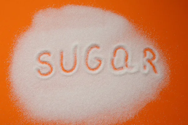 オレンジの背景に砂糖の砂の上に碑文シュガー 白砂糖の山に書かれた砂糖という言葉 — ストック写真