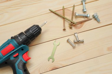 Ahşap masadaki aletler, matkap uçları ve cıvatalı vidaları olan elektrikli bir tornavida. Diy konsepti. Ekipman, iş yeri. Düz konum.