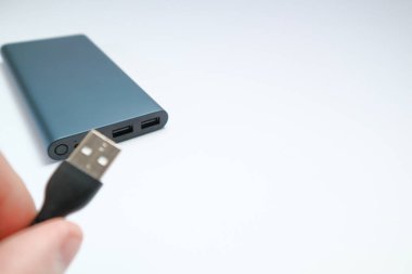 USB kablosunu güç bankasına bağlıyorum. El ele tutuşan USB kablosu ve gri güç bankası. Akıllı telefon için güç tasarrufu aygıtı güç bankası.
