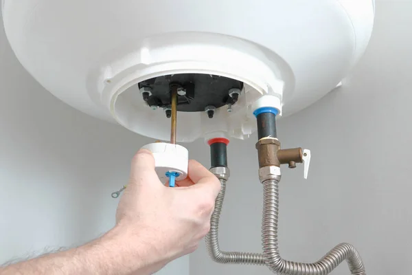 The hand of a plumber installs a thermostat in a boiler after repair. Water heater repair.