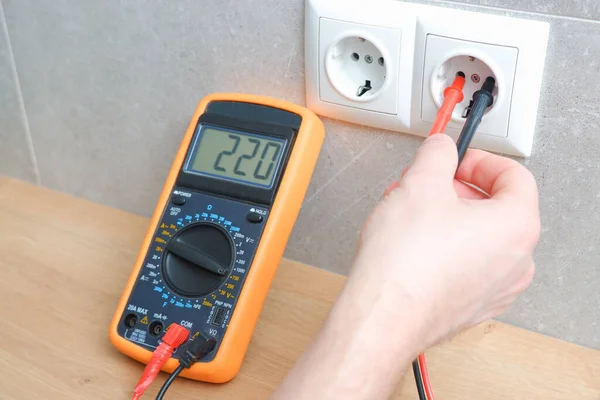 The electrician measures the voltage in the home network by inserting a voltmeter into the outlet. Measurement of voltage in electric networks