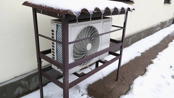 Heat pump mounted onto the wall of a house and covered in snow on a cold winters day.