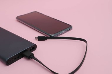 Powerbank charging a smartphone. Smartphone battery charging from portable powerbank with white usb cable.