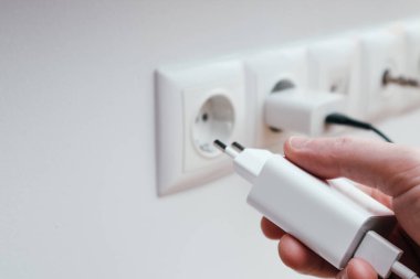Man hands plugging the charger into an outlet in the wall, close-up