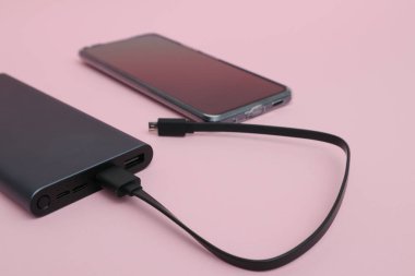 Powerbank charging a smartphone. Smartphone battery charging from portable powerbank with white usb cable.