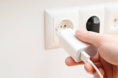 Man hands plugging the charger into an outlet in the wall, close-up