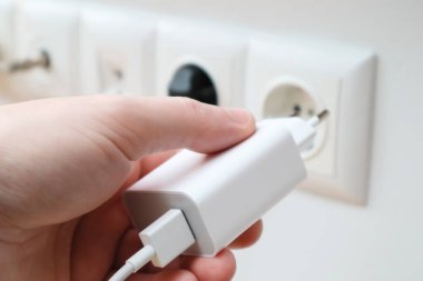 Man hands plugging the charger into an outlet in the wall, close-up