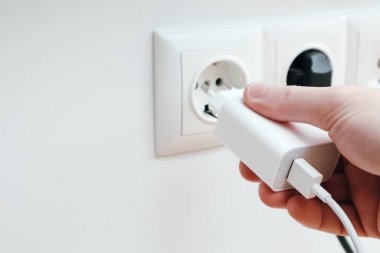 Man hands plugging the charger into an outlet in the wall, close-up
