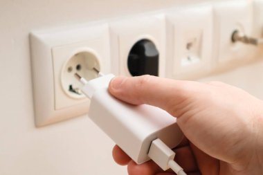 Man hands plugging the charger into an outlet in the wall, close-up