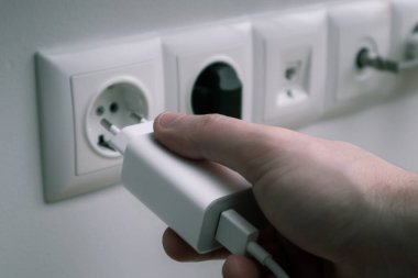 Man hands plugging the charger into an outlet in the wall, close-up
