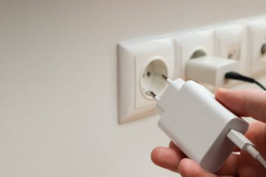 Man hands plugging the charger into an outlet in the wall, close-up