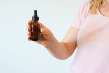 Women's hands hold bottle of amber glass with cosmetic face serum on white background. Young woman holding brown glass bottle with dropper with spa cosmetics.