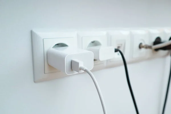 Many chargers plugged into maltiple electrical outlet on white background. Concept of power use in residence, office or home with safety and saving.