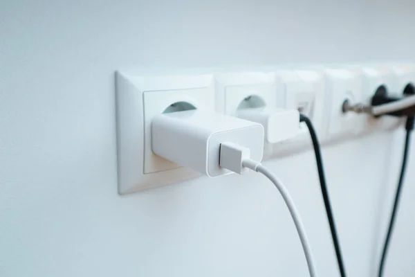 Many chargers plugged into maltiple electrical outlet on white background. Concept of power use in residence, office or home with safety and saving.