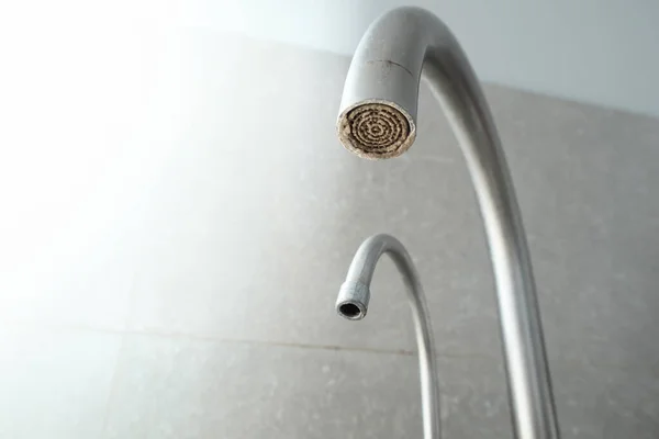 Selective focus on hard water deposit. Dirty faucet aerator with limescale, calcified shower water tap with lime scale in the kitchen, close up. A heavily calcified faucet