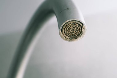 Selective focus on hard water deposit. Dirty faucet aerator with limescale, calcified shower water tap with lime scale in the kitchen, close up. A heavily calcified faucet clipart