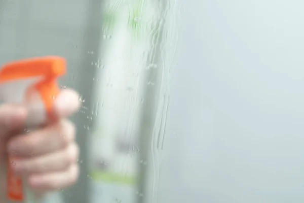 Hand holding glass cleanser spray. Hand sprays detergent on the mirror. spraying liquid to the glass.