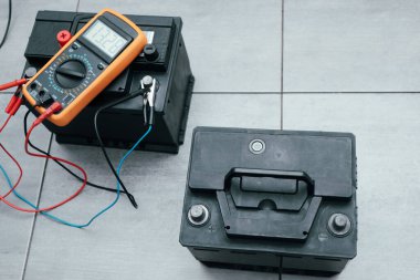 Check and charge car battery with charger. Person measures voltage. Selective focus an auto mechanic uses a multimeter voltmeter to check the voltage level in a car battery.