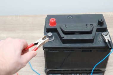 Close up of hand Charging car battery with electricity trough jumper cables. Electrical charging Cables on a 12 volt Battery