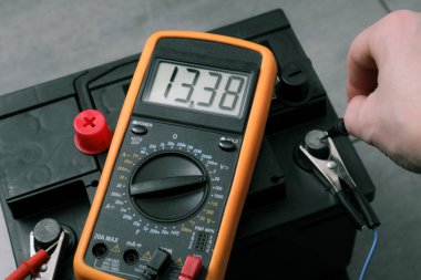 Check and charge car battery with charger. Person measures voltage. Selective focus an auto mechanic uses a multimeter voltmeter to check the voltage level in a car battery.