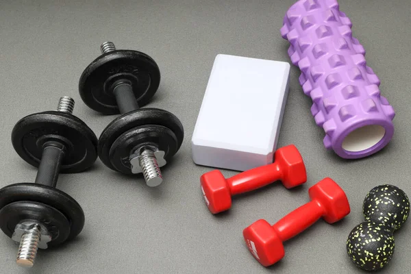 Foam rollers, dumbbells and yoga block on grey mat with massage roller. Set of fitness equipment. Tool for back tension and muscle pain release - physical therapy and training stretch concept