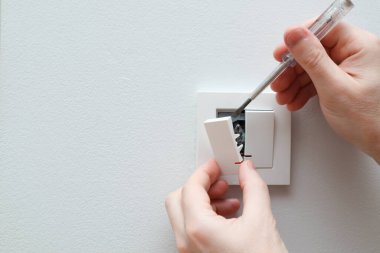 Bir elektrikçi bir elektrik düğmesini değiştiriyor. Bir DIY proje konsepti. Yüksek voltaj tehlikesi. Elektrikçi, duvar lambasını tamir ediyor..