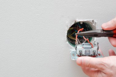 Bir elektrikçi bir elektrik düğmesini değiştiriyor. Bir DIY proje konsepti. Yüksek voltaj tehlikesi. Elektrikçi, duvar lambasını tamir ediyor..
