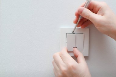 Bir elektrikçi bir elektrik düğmesini değiştiriyor. Bir DIY proje konsepti. Yüksek voltaj tehlikesi. Elektrikçi, duvar lambasını tamir ediyor..