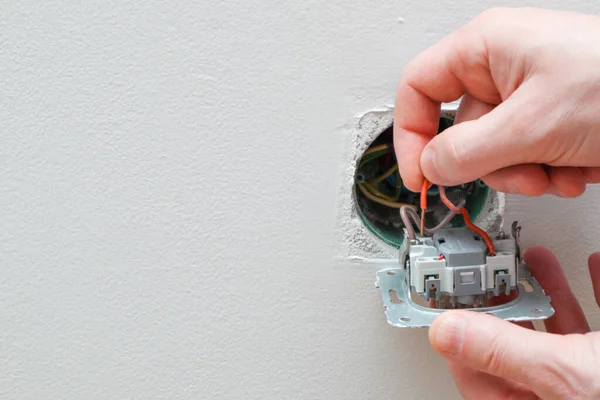 Bir elektrikçi bir elektrik düğmesini değiştiriyor. Bir DIY proje konsepti. Yüksek voltaj tehlikesi. Elektrikçi, duvar lambasını tamir ediyor..
