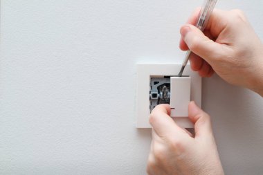 Bir elektrikçi bir elektrik düğmesini değiştiriyor. Bir DIY proje konsepti. Yüksek voltaj tehlikesi. Elektrikçi, duvar lambasını tamir ediyor..