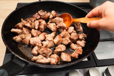 Eti kızartma tavasında karıştıran bir kadın. Kızarmış et, patates kızartması. Sığır pirzolası hazırlarken bir tavayı kapat.