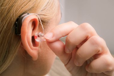 Kadının işitme cihazını kulağına sokmasına yakın çekim. Modern işitme cihazlı sarışın kadın. İşitme engelli.
