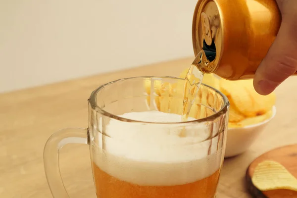 Canned beer pouring into mug. Hand pouring a beer can into a beer jug. Womans Hand holding yellow aluminium can, pouring beer.