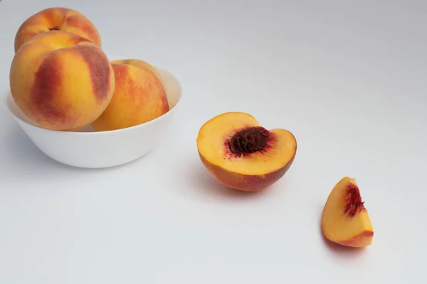 Fresh ripe peaches in a white plate, half and a quarter of a peach on a white background. Delicious and healthy food. Organic vitamins for dessert.