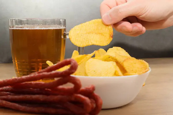 A man\'s hand takes snacks next to beer. Beer snack. Dry thin meat sausages and chips. Man drinking beer and eating snacks