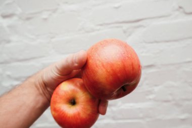 Beyaz tuğlalı arka planda elinde organik kırmızı elma tutan adam. Meyveler, sağlıklı yiyecekler, organik yiyecekler ve insanlar konsepti. Elma tutan adamı yakından çek..